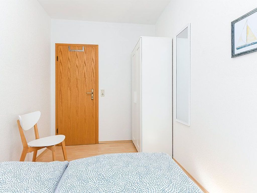 Una habitación pequeña y limpia con una puerta de madera, una silla blanca y una cama con edredón estampado.