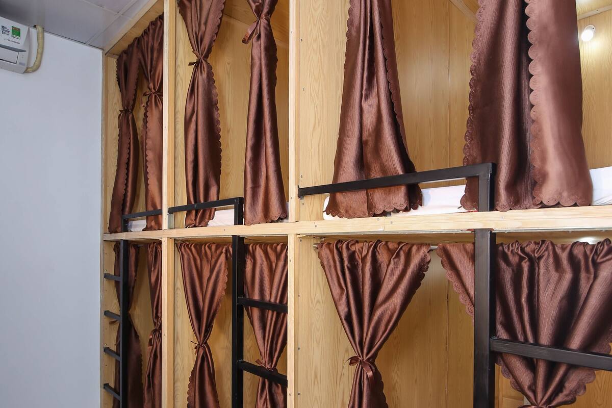 A dormitory room with bunk beds, wooden headboards, and curtains tied at the top.