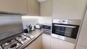 A modern kitchen with a gas stove, a built-in oven, a microwave, and a toaster. - The Central Lodge II (Dartford)