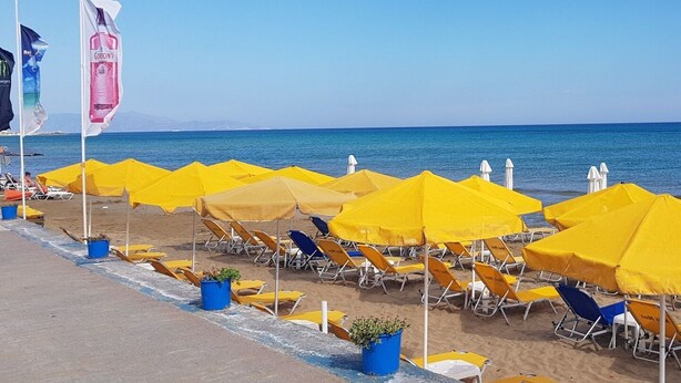 A beach with rows of yellow umbrellas and lounge chairs, a clear blue sky, and the sea in the background. - Beachfront Apartments in Gouves (Hersonissos)