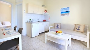A compact living space with a kitchenette, a dining area, and a seating area with a sofa and cushions. - Beachfront Apartments in Gouves (Hersonissos)