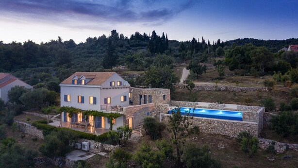 A villa with a swimming pool, surrounded by trees and hills.