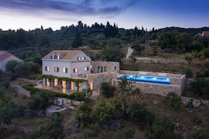 A villa with a swimming pool, surrounded by trees and hills.