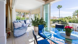 Un balcon avec une table en verre, des chaises bleues et un canapé agrémenté de coussins à motifs.