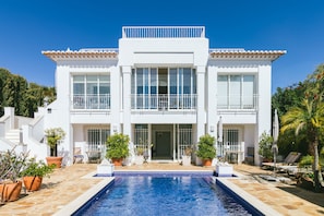 A two-story building with a swimming pool in front, surrounded by potted plants and outdoor furniture. - Fantastically beautiful villa with pool and sea view (Albufeira)