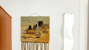 A room with a wooden cabinet, a tapestry with a maritime scene, and a wavy mirror reflecting a dining area. - APARTMENT IN SEA VIEW RESIDENCE, 200 METERS FROM THE BEACH WI FI (Alcamo)