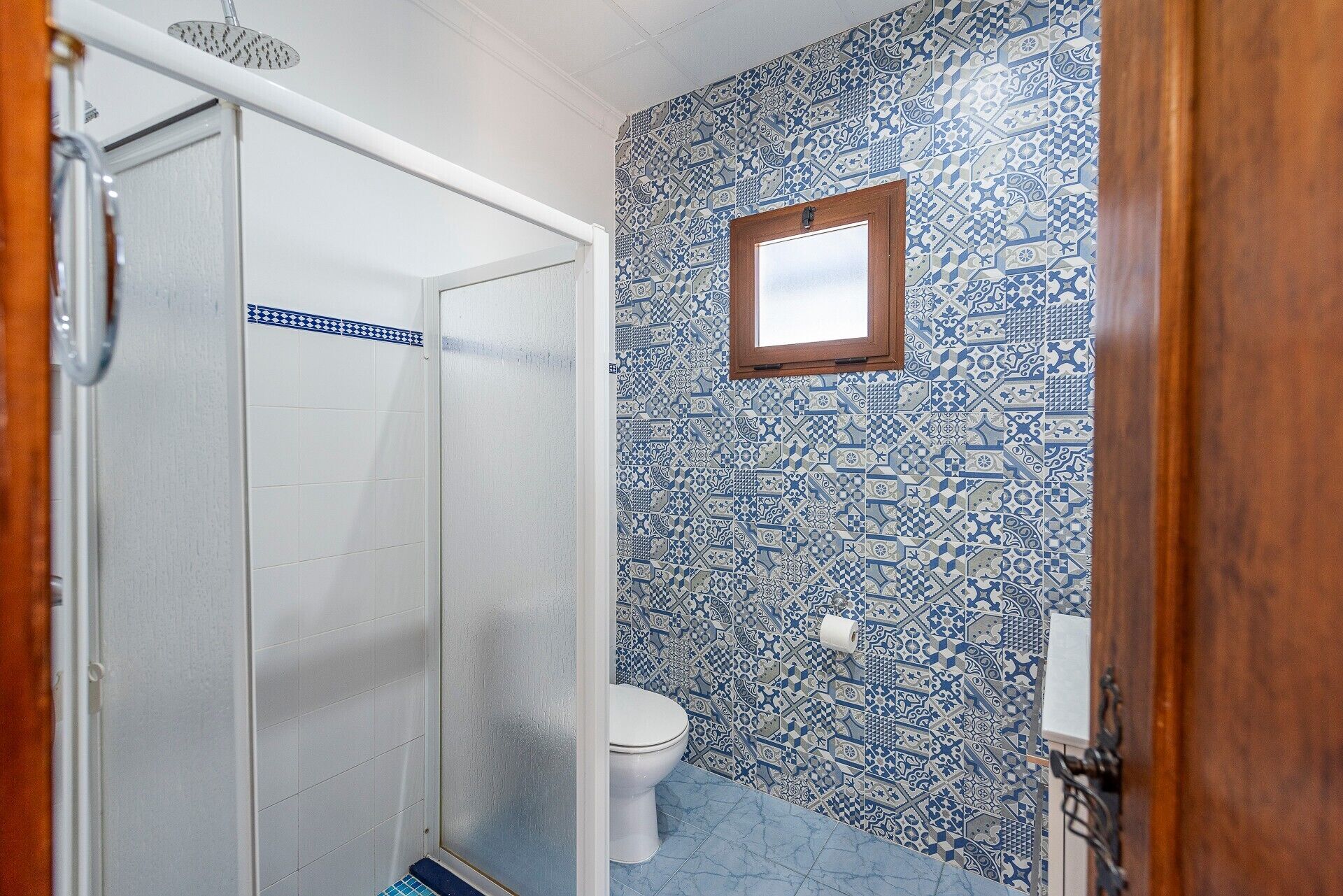 A bathroom with a shower, toilet, and patterned tiles.