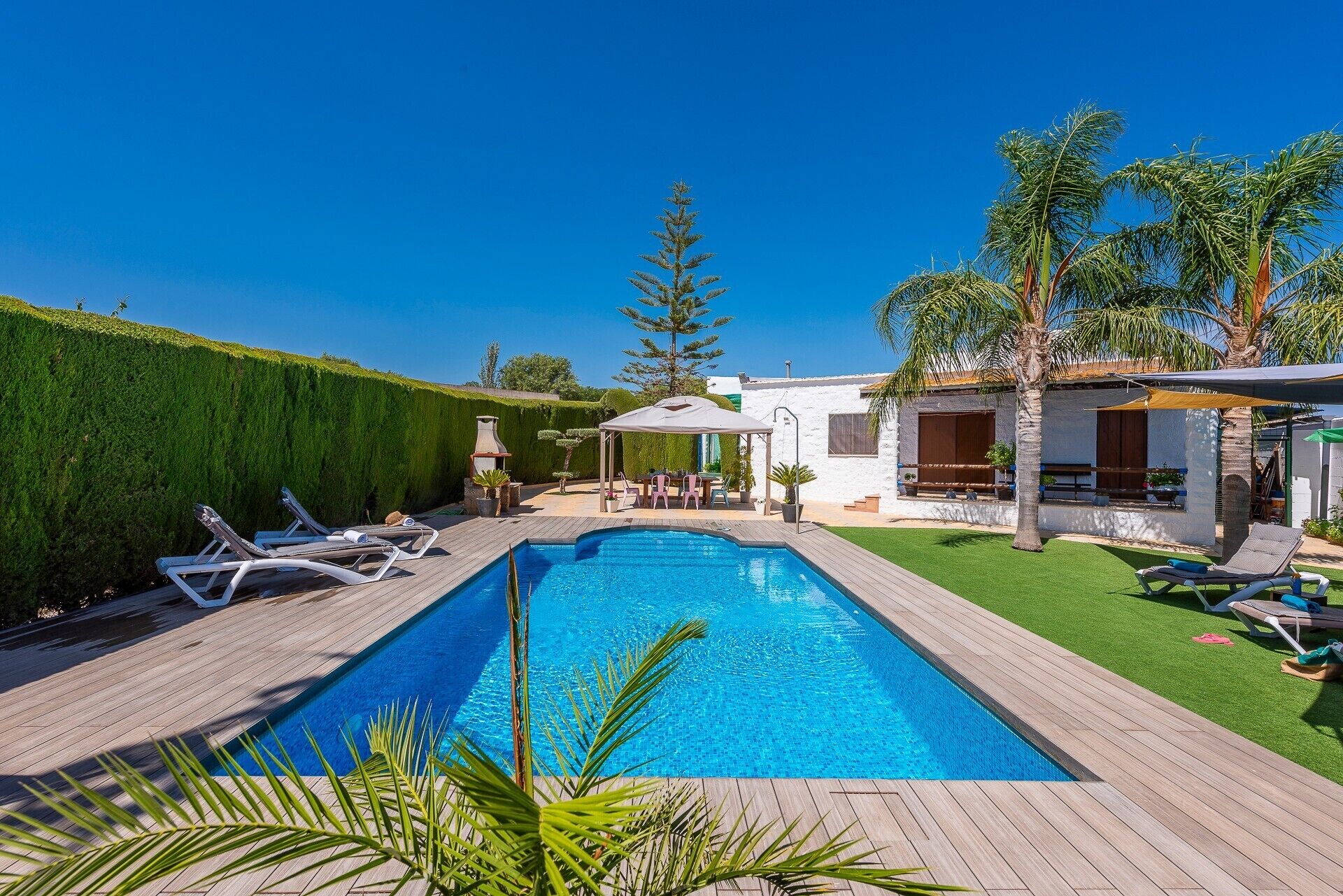 A rectangular swimming pool with a wooden deck, surrounded by a well-maintained lawn and a white building with windows.