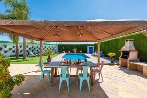 Un patio exterior con piscina, una parrilla y un comedor cubierto.