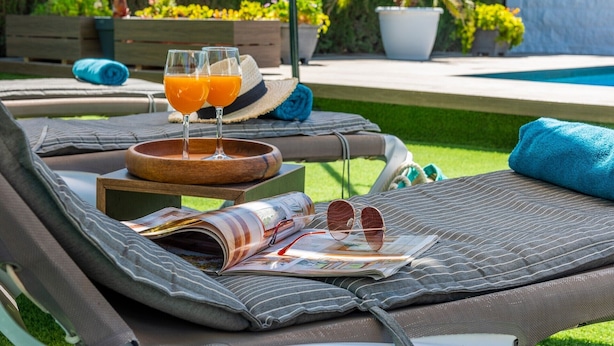 Un fauteuil confortable avec un magazine, des lunettes de soleil et deux verres de jus d’orange.