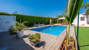 Une piscine entourée de chaises longues, de plantes en pot et d’un mur blanc agrémenté d’une haie.