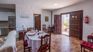 Un coin repas avec une table blanche dressée pour quatre personnes, une cuisine équipée d’un réfrigérateur en acier inoxydable, un extincteur fixé au mur et une porte donnant sur l’extérieur.