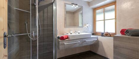 A modern bathroom with a glass shower enclosure, a large mirror, a sink with a vanity, and a toilet.