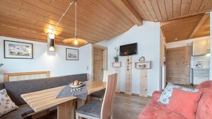 A cozy living space with a wooden dining table, a sofa, and a TV mounted on the wall.