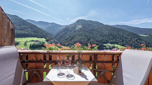 A table with wine glasses and a bottle, set against a mountainous backdrop.
