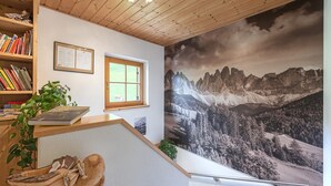 A room with a wooden ceiling, a bookshelf, a framed certificate, a window, and a large mountain landscape mural.