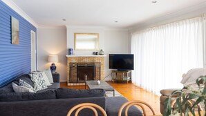 Sala de estar com sofá, televisão, lareira e uma janela grande com cortinas.