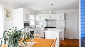 Uma cozinha moderna com armários brancos, fogão, micro-ondas e torradeira. Há uma mesa de jantar com cadeiras e uma planta sobre a mesa.