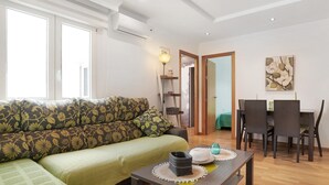 Una sala de estar con un sofá, una mesa de comedor con sillas, una lámpara y un cuadro en la pared.