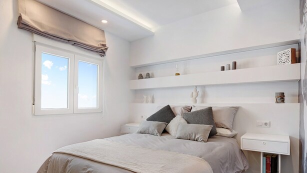 Un dormitorio con cama, mesitas de noche, ventana y estanterías empotradas.