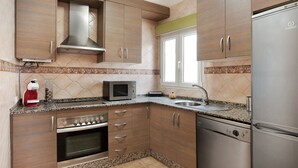 Una cocina con gabinetes de madera, campana de acero inoxidable, microondas, lavavajillas y refrigerador.