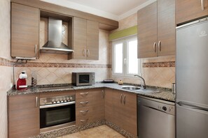 A kitchen with wooden cabinets, a stainless steel range hood, a microwave, a dishwasher, and a refrigerator.
