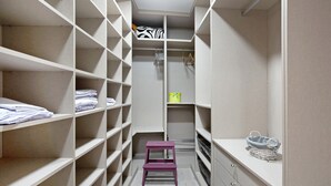 Un vestidor amplio con varias estanterías, un taburete y una cesta a la derecha.