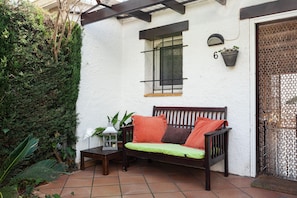 Un patio con un banco de madera, una planta en maceta y un letrero numérico en la pared.