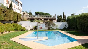 Una piscina rettangolare con bordo piastrellato, circondata da erba e siepi, con un edificio sullo sfondo.