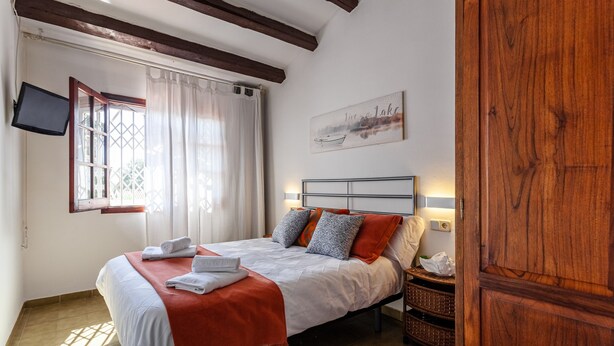 Una camera da letto con un letto, una TV a parete, una finestra con tende e una porta in legno.