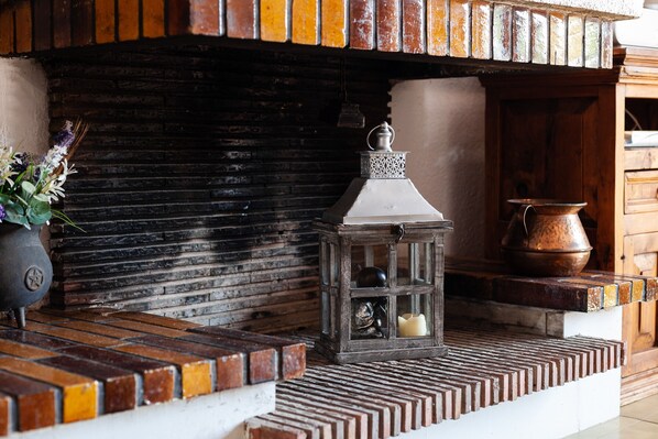 A rustic fireplace with a lantern, a potted plant, and a copper pot.