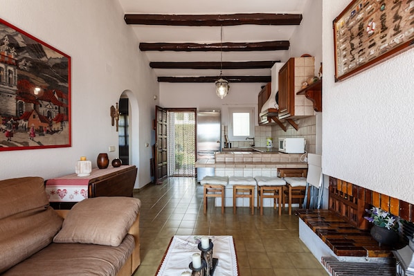 Una sala de estar acogedora con un sofá, un comedor con mesa y sillas, una cocina con microondas, y una escalera que lleva a otro nivel.