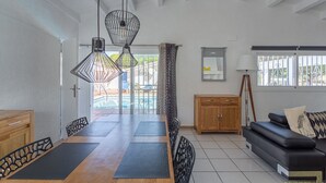 A dining area with a wooden table, black chairs, and a black sofa with a patterned pillow. There are two pendant lights above the table. - Villa 'Sea près des golfs-El Sol Naciente' with Mountain View, Pool and Wi-Fi (Santa Cristina d'Aro)