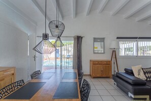 Uma sala de jantar com mesa de madeira, cadeiras pretas e um sofá preto com almofada estampada. Há duas luminárias pendentes sobre a mesa.