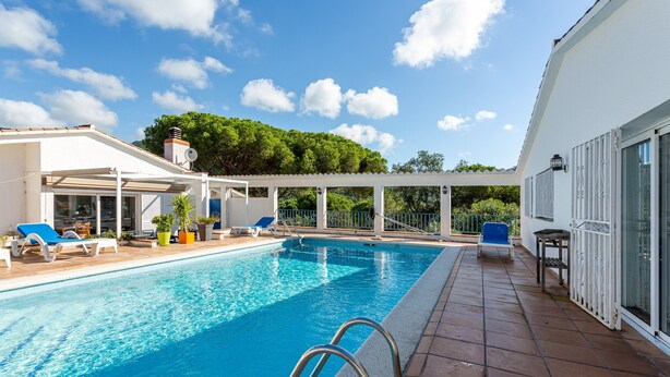 A swimming pool with sun loungers, a covered patio area, and a view of trees in the background. - Villa 'Sea près des golfs-El Sol Naciente' with Mountain View, Pool and Wi-Fi (Santa Cristina d'Aro)