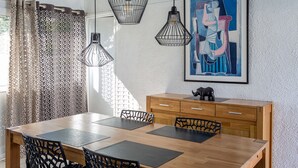 A dining area with a wooden table, chairs, hanging pendant lights, a cabinet, and a framed artwork on the wall. - Villa 'Sea près des golfs-El Sol Naciente' with Mountain View, Pool and Wi-Fi (Santa Cristina d'Aro)
