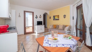 Un comedor con una mesa lista para dos personas, una cocina con un electrodoméstico rojo, un televisor y una cama con almohadas.