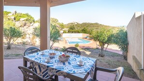 Un patio techado con una mesa lista para comer, con vista a una piscina y un paisaje montañoso.
