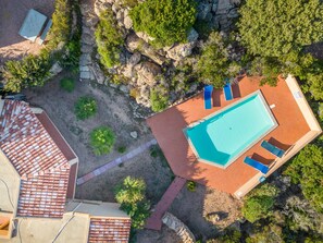 An aerial view of a property with a swimming pool, lounge chairs, and a tiled roof.