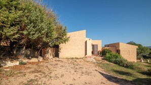 Un edificio de estilo desértico con un sendero de tierra que conduce a la entrada, rodeado de vegetación escasa y un cielo azul despejado.