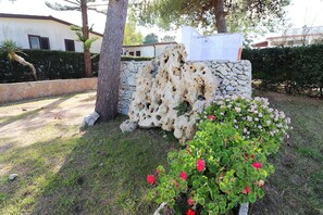 Un mur de pierres percé de trous, un arbre et un parterre de fleurs roses.