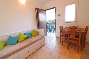 A room with a sofa, a dining table with chairs, a window, and a door leading outside.