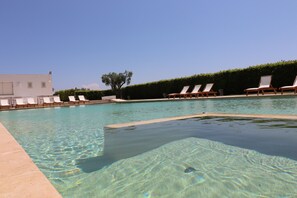 A clear swimming pool with lounge chairs and a hedge in the background.