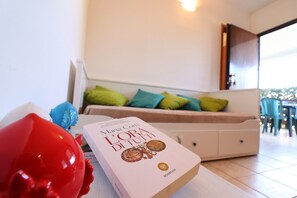 Un libro titulado 'L'ora di tutti' sobre una mesa en una habitación con un sofá, almohadas y vistas al exterior.