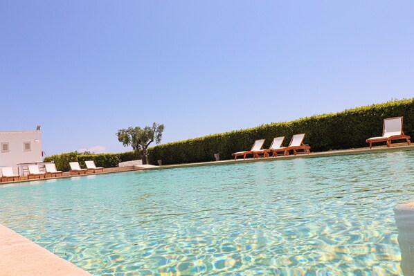 Una piscina cristalina con sillas de descanso y un seto.