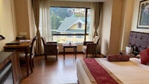 A hotel room with a bed, a desk, two chairs, a window with a view of buildings, and a fireplace. - Zone Connect Darjeeling (Darjeeling)