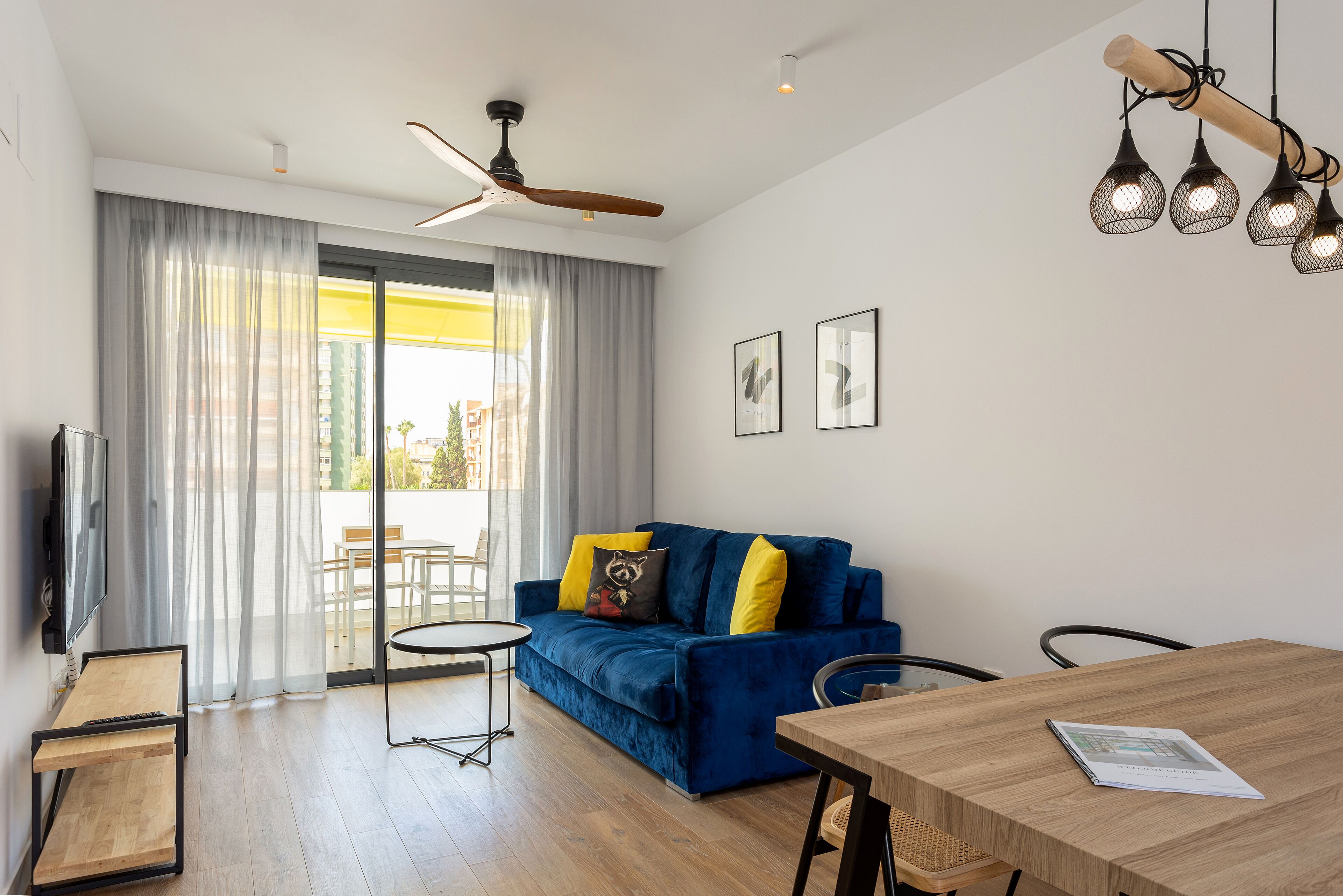 Een moderne woonkamer met een blauwe bank, een houten eettafel en een plafondventilator.
