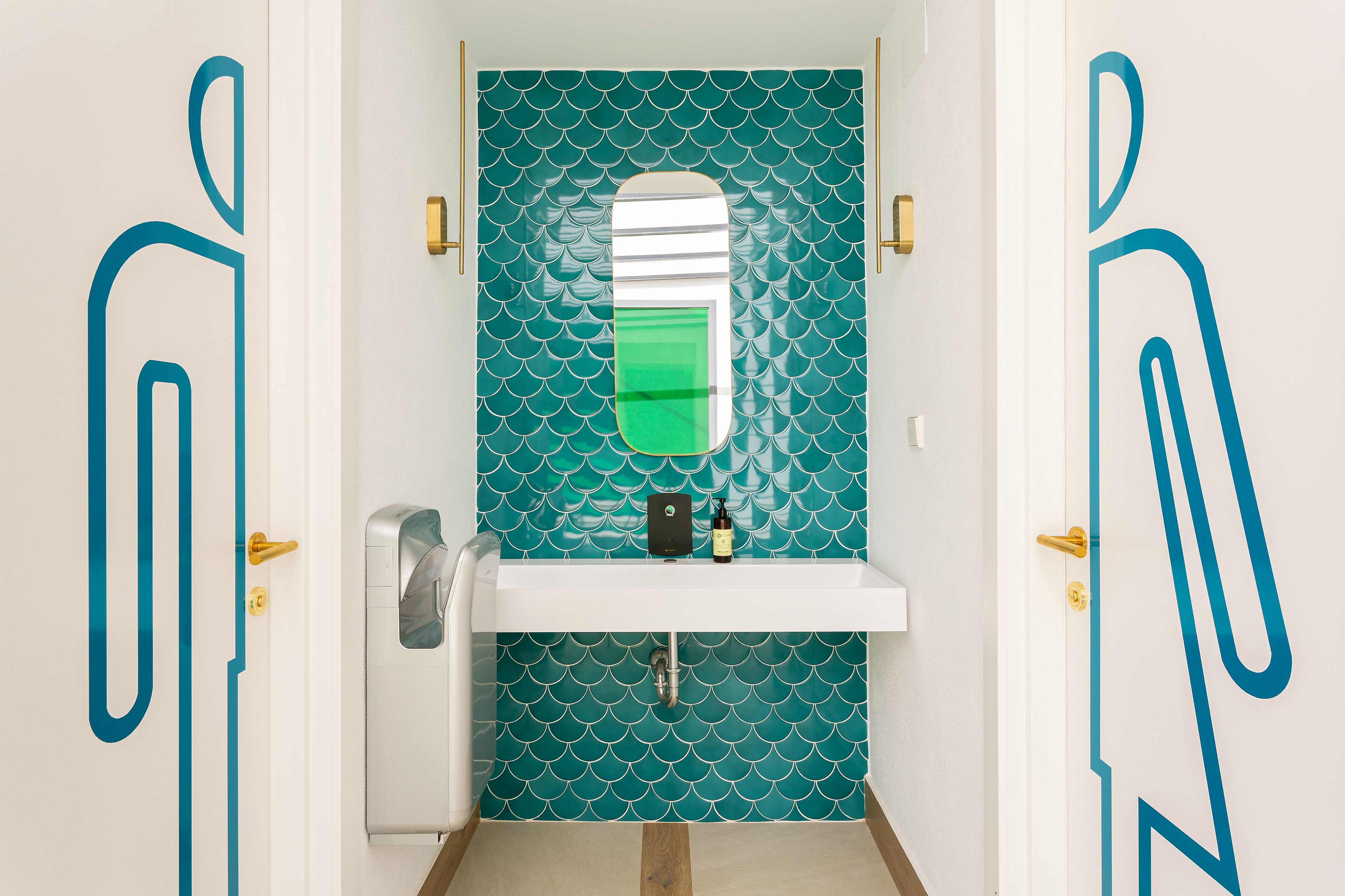 A bathroom with teal patterned tiles, a white sink, and a mirror.