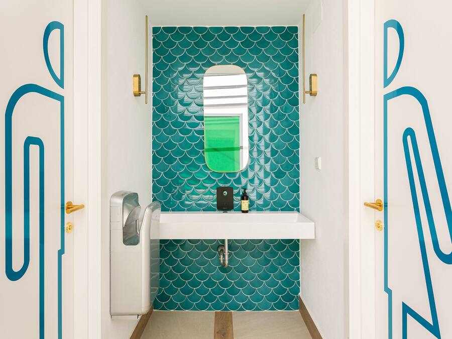 A bathroom with teal patterned tiles, a white sink, and a mirror.