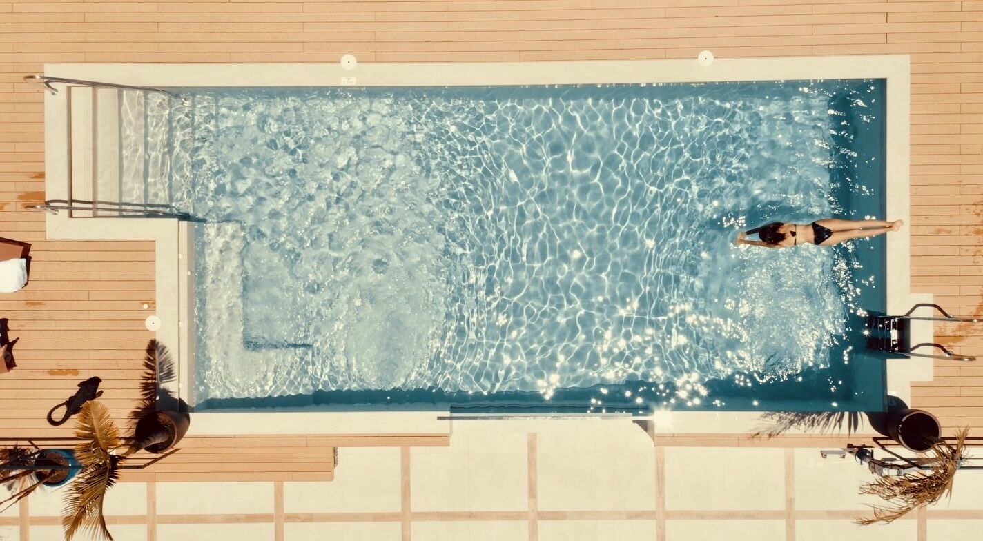 Una piscina rectangular de aguas cristalinas, rodeada por un deck de madera y equipada con una escalera y un trampolín.